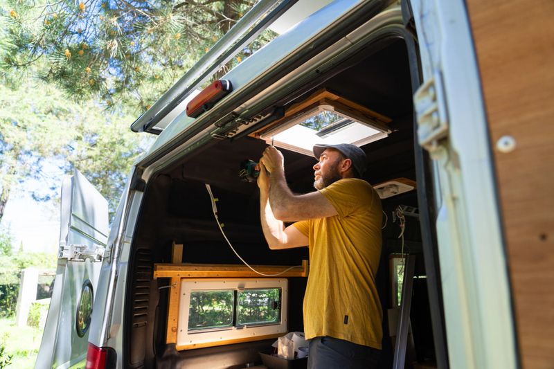 Skilled technician installing a new roof window in a campervan, enhancing natural light and ventilation during outdoor adventures