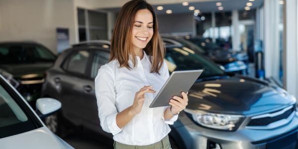 Woman smiling and using tablet in car showroom.