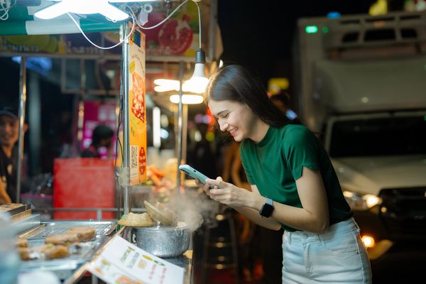 A woman enjoying street food at night, smiling while taking a photo.
