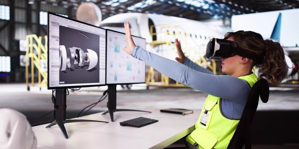 Woman using virtual reality to interact with aircraft engine design on dual monitors.