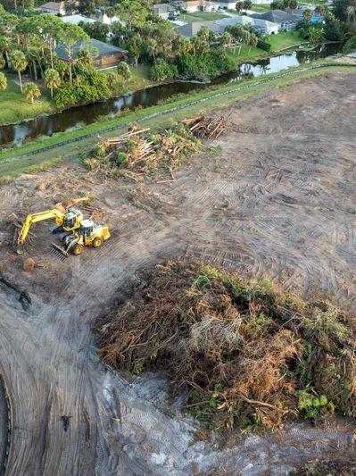 Excavators clearing land near a canal, surrounded by residential homes.