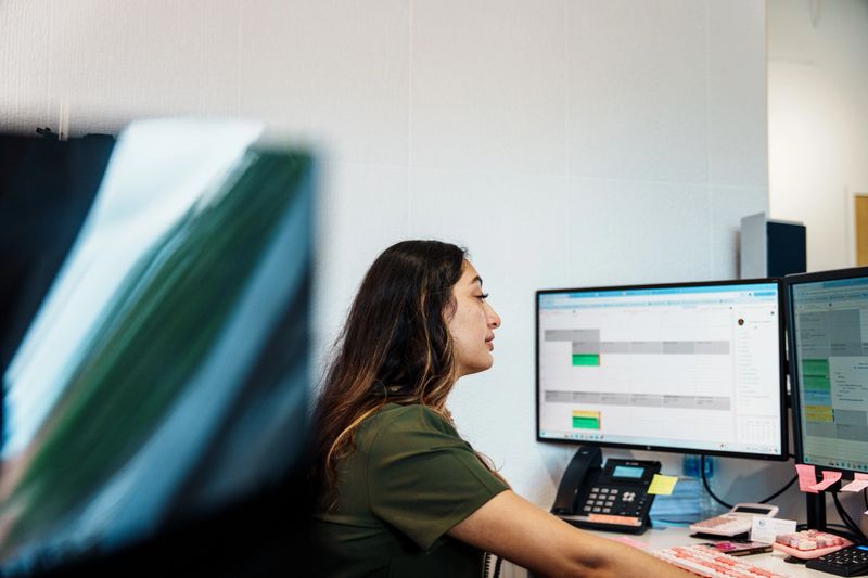 A woman of Hispanic descent who works at the reception desk in a dental clinic works on the computer while scheduling patients.