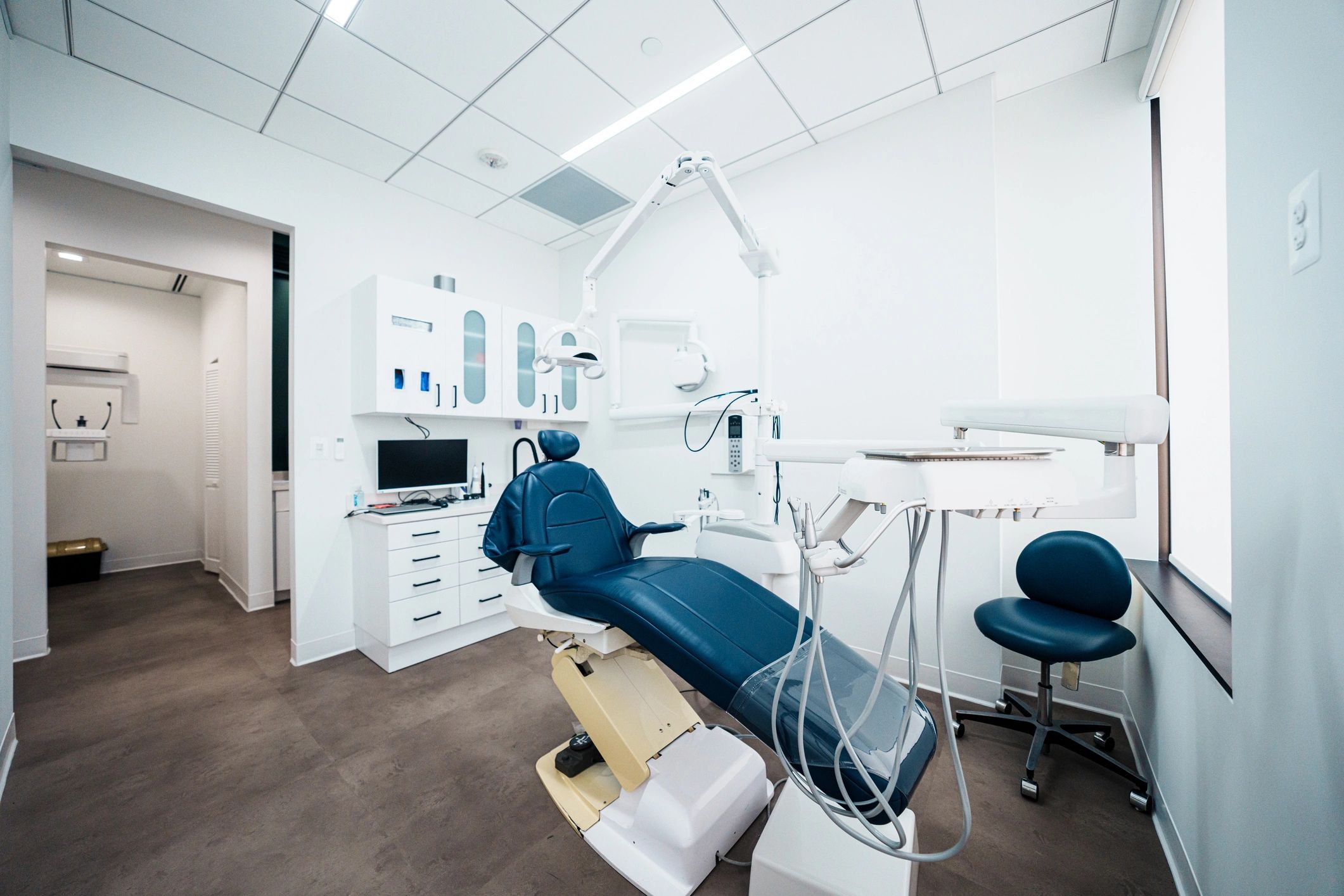 Modern dental clinic room with blue dental chair and equipment.