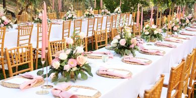Elegant outdoor wedding table setup with floral centerpieces and wooden chairs.