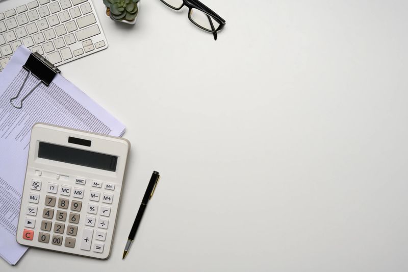 Top view of a tidy workspace with calculator, keyboard, glasses and a stack of documents.