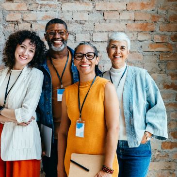Diverse group of four professionals smiling against a brick wall.