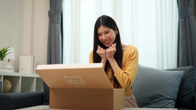 Smiling Asian Woman Unpacking a Fashion Bag in Her Living Room - Lifestyle Excitement, Consumer Engagement, and Online Shopping Success with Wireless Technology and Social Media Connection
