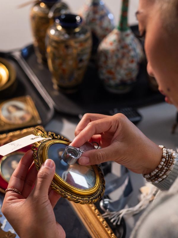 Person examining an ornate framed picture with a magnifying glass.