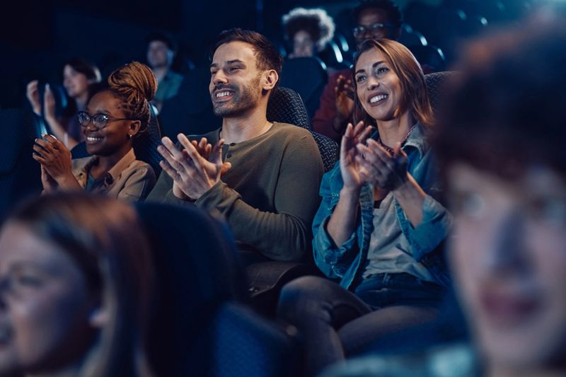 Group of happy people applauding after film screening at movie theatre.