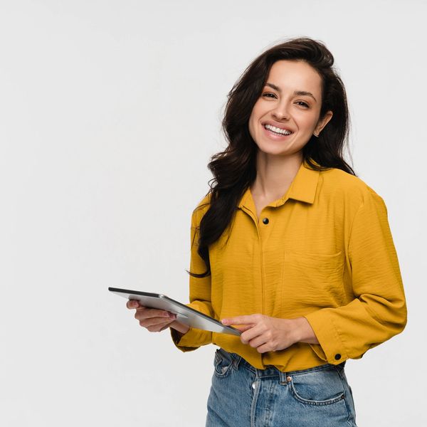 Smiling woman in yellow shirt holding a tablet.