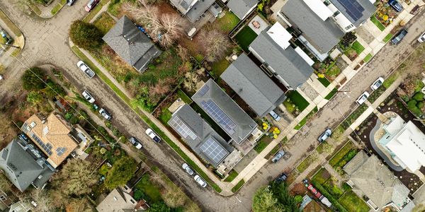 Aerial view of a suburban neighborhood with houses, solar panels, and parked cars.