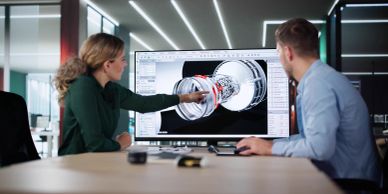 Two designers analyze a 3D model on a computer screen.
