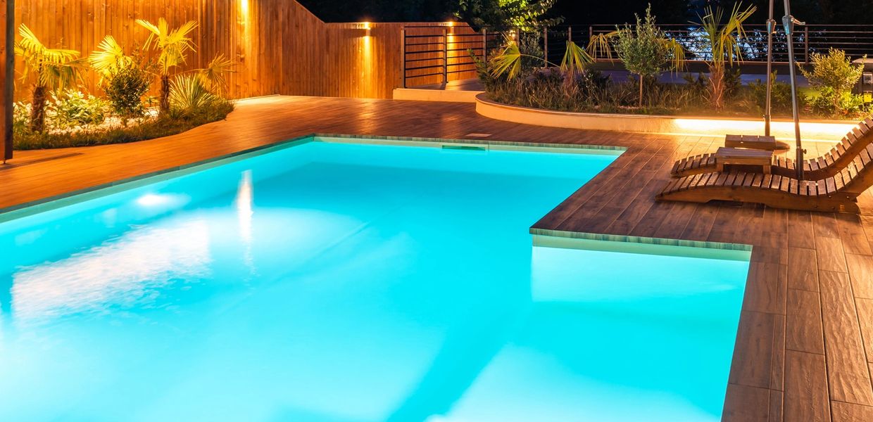 A beautifully lit backyard pool area with lounge chairs and an umbrella at dusk.