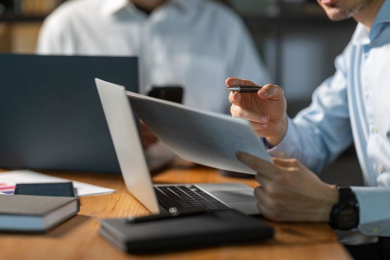 Businessman reviewing documents and working on a laptop during an office meeting, showcasing professionalism and fostering collaboration among team members in a corporate environment