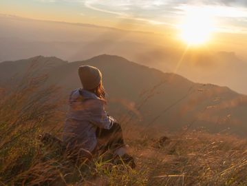 A person sitting on a hill watching a golden sunset over misty mountains.