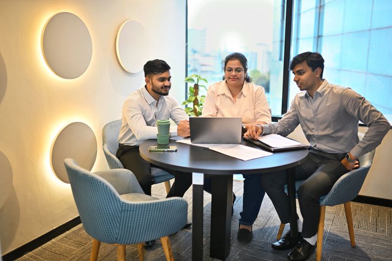 A professional mid-adult manager engages in a lively discussion with a group of diverse interns in a sleek, modern meeting room. The room features large windows, natural lighting, and minimalist decor, emphasizing a collaborative and innovative workplace environment. The manager gestures while explaining a concept, and the interns attentively take notes and ask questions, showcasing teamwork and mentorship.