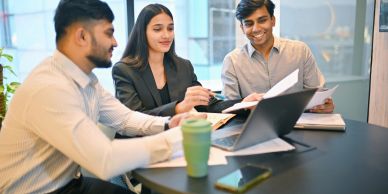Three professionals collaborating around a table with documents and a laptop.