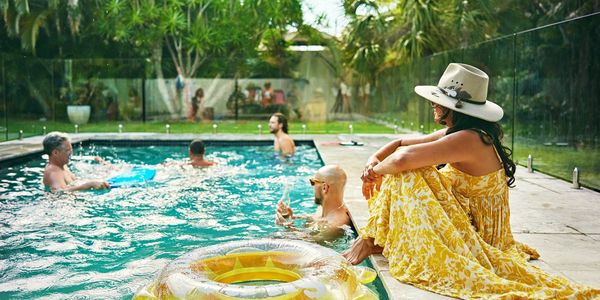 Woman in yellow dress sitting by the pool while others swim and relax.