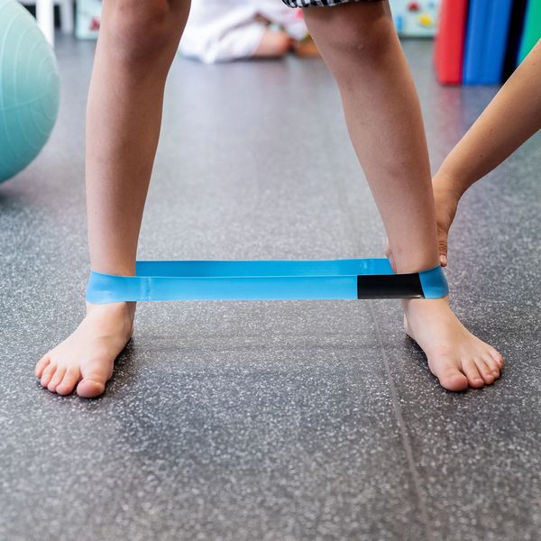 Child doing leg resistance exercise with blue band.