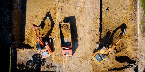 Aerial view of two excavators loading dirt into a dump truck on a construction site.