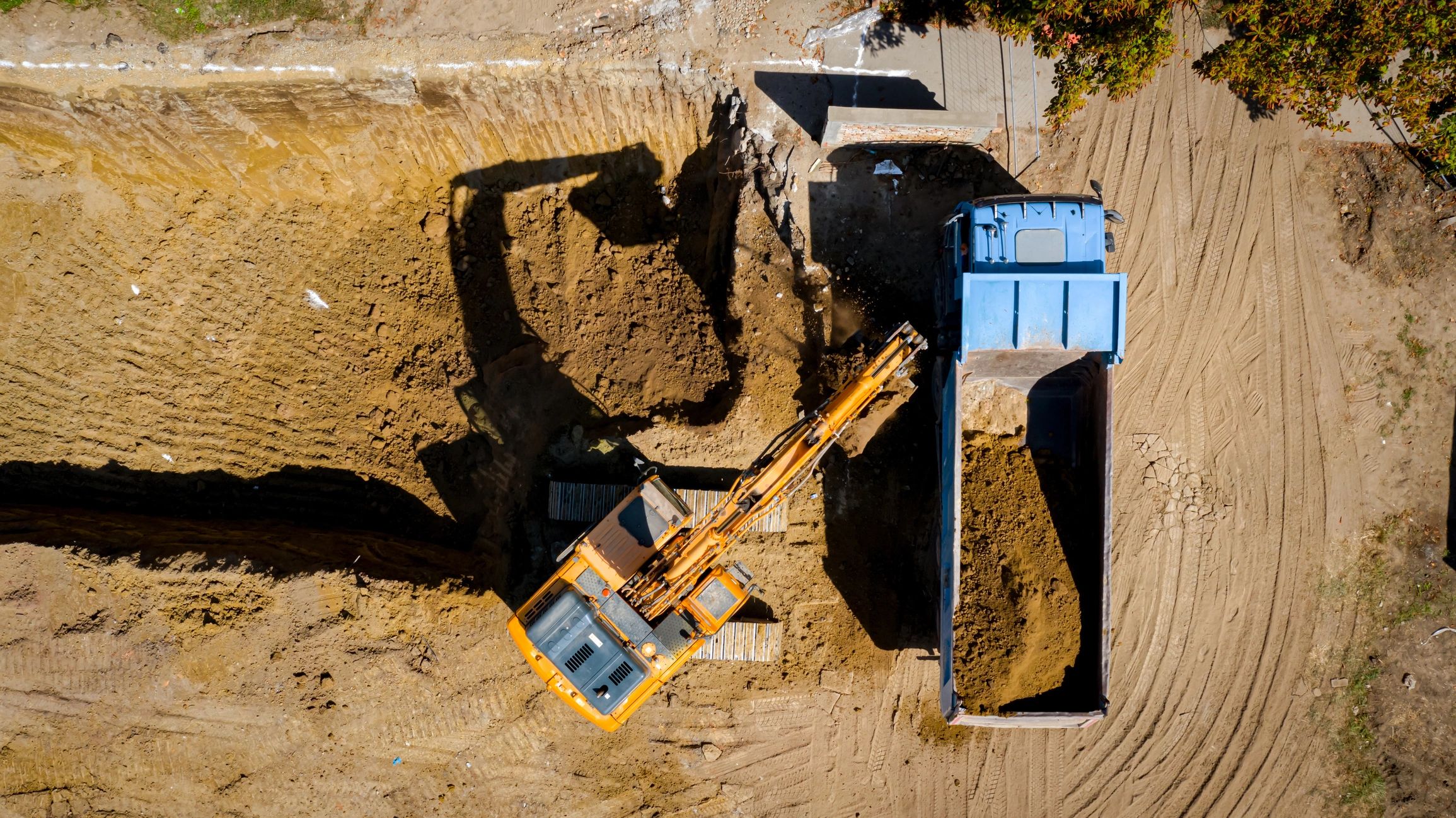 Excavator loading dirt into a blue dump truck.