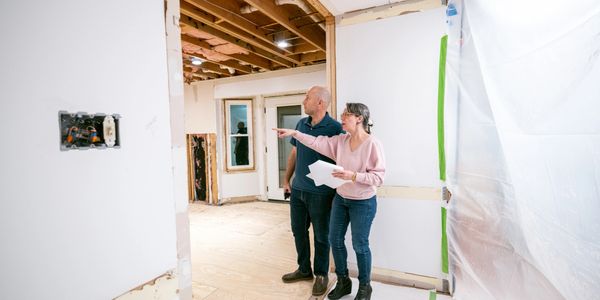 A couple discusses home renovation plans in an unfinished room.