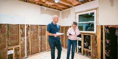 Couple discussing home renovation in an unfinished room with exposed insulation and wiring.