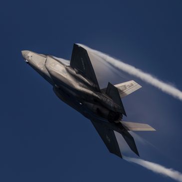 A U.S. Marines F-35 fighter jet flying at high speed with vapor trails.