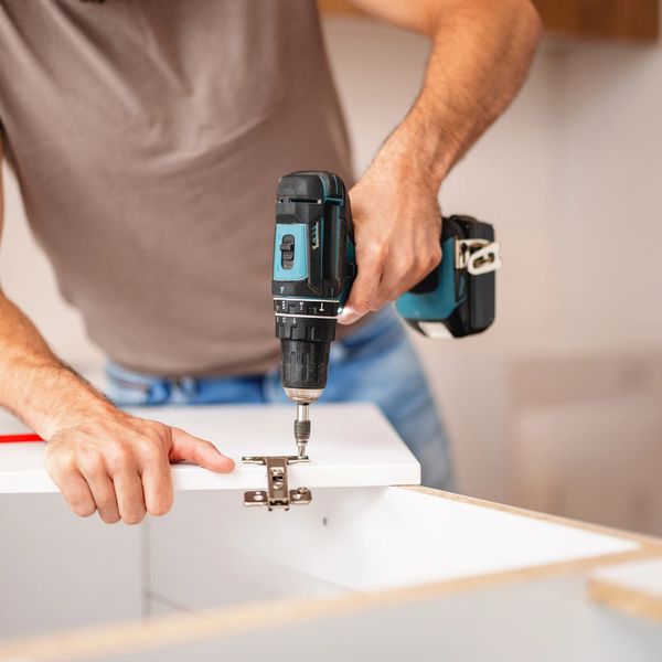 Person using a cordless drill to install a hinge on a cabinet door.