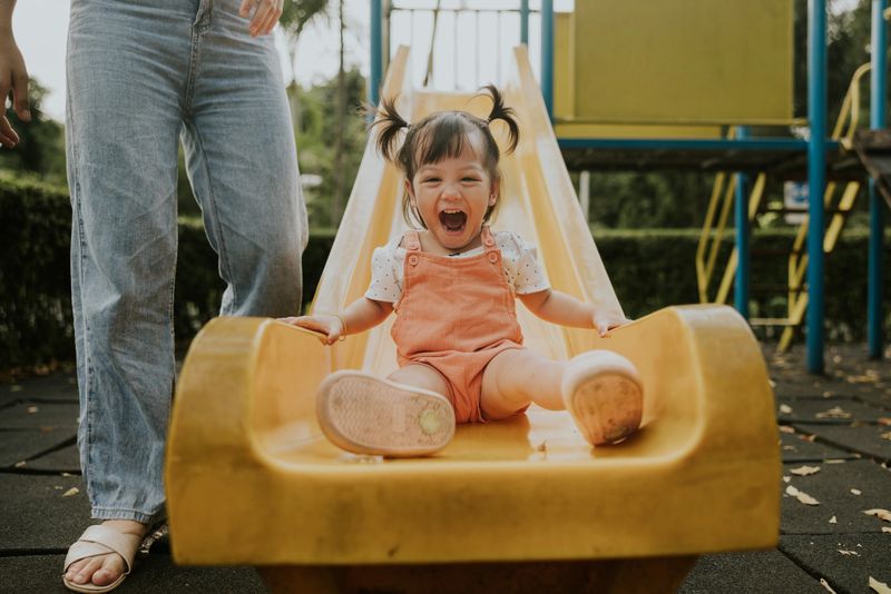 Excite moment of Smiling of cute girl while playing slider, sliding equipment for relaxation beside her mother
