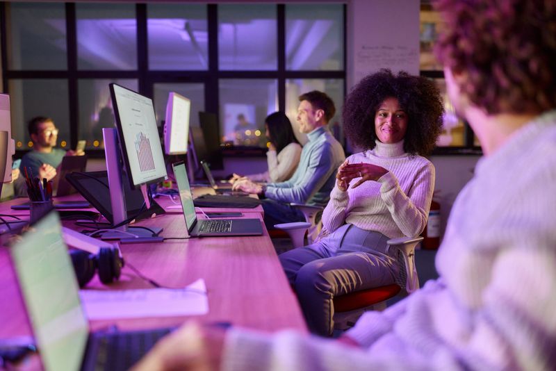 Smiling African American graphic designer communicating with her colleague while working late in the office.