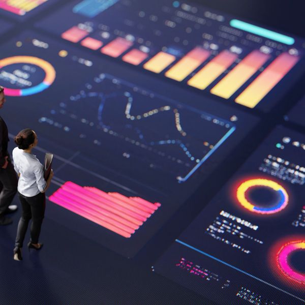 Two professionals analyzing vibrant data visualizations on a large digital interface.