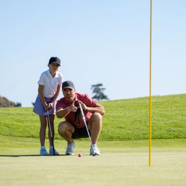 A man and a girl lining up a golf putt on the green.