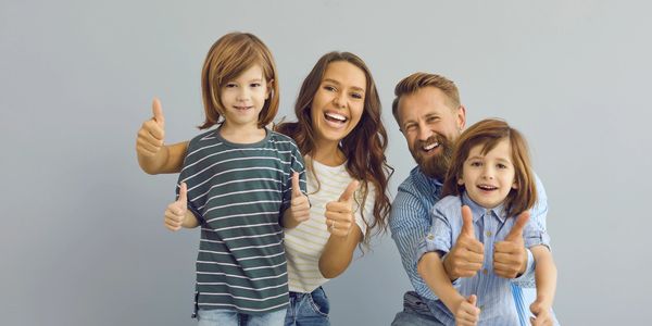 Happy family of four giving thumbs up and smiling.
