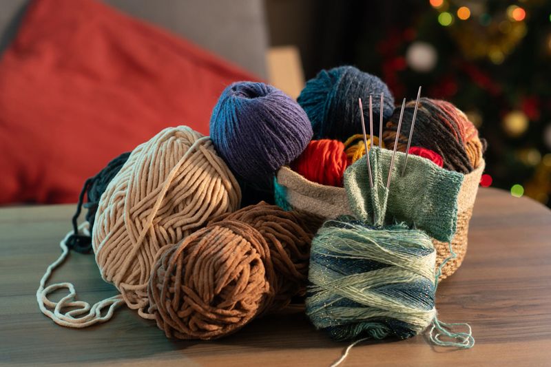 A collection of colorful yarn balls and knitting supplies neatly arranged on a table, set against a cozy background with festive lights and a Christmas tree