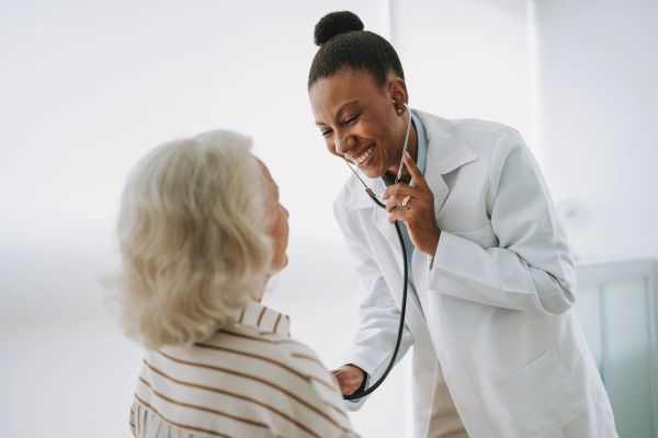 Doctor smiling at elderly patient with a stethoscope.