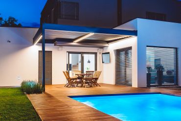 A poolside pavilion with stone walls and wooden beams reflected in the water.