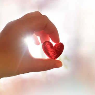 Hand holding a small red heart against sunlight.