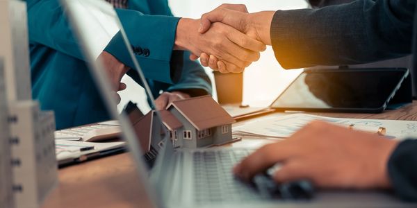 two people shaking hands near a laptop computer