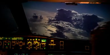 View from an airplane cockpit showing illuminated controls and dark clouds outside.