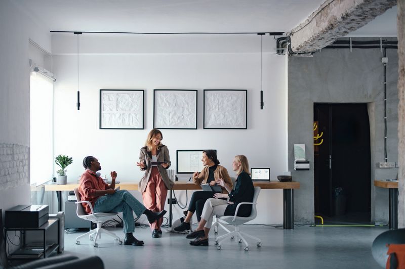 A group of coworkers discussing projects in a relaxed, contemporary workspace setting.
