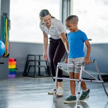 Child learning to walk with a walker assisted by a supportive adult.