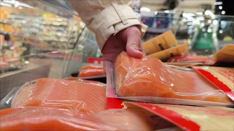 Woman Customer Choosing Fresh Salmon In Supermarket. Close Up. The buyer's hand chooses a package of fresh salmon fish in the supermarket.