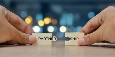 Two hands connecting puzzle pieces labeled 'PARTNER' and 'SHIP' symbolizing partnership.