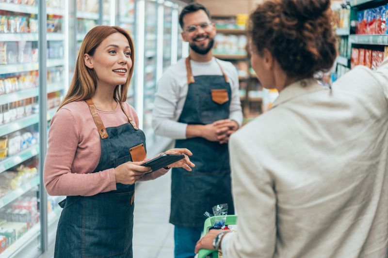 Retail clerk helping a woman shopping at the supermarket. Young shop assistant helping female customer in grocery store. Saleswoman assisting shopper in supermarket. Woman talking to supermarket worker while buying groceries