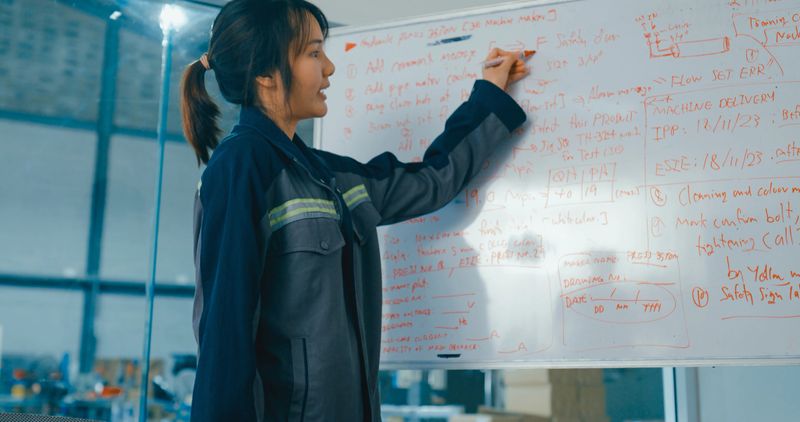 Group of engineers having meeting in factory, using whiteboard for discussing project details and planning. Robotic Industrial Factory Concept.