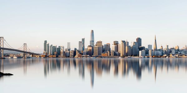 San Francisco skyline with Bay Bridge and calm water reflections.