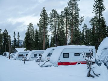 Snow-covered caravans parked in a winter forest setting. Winterized