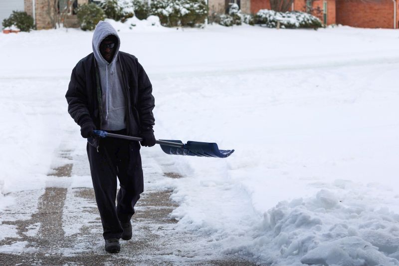 A portrait of a black man shoveling a driveway