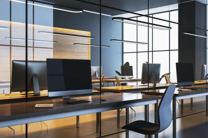 Stylish office interior with computers on wooden desks, chairs, glass partitions, and natural light. Concept of a modern workplace design. 3D Rendering.